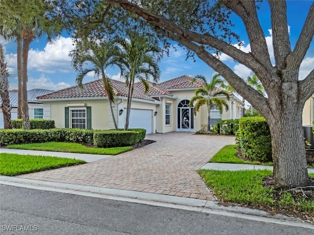 mediterranean / spanish house with stucco siding, an attached garage, driveway, and a tile roof