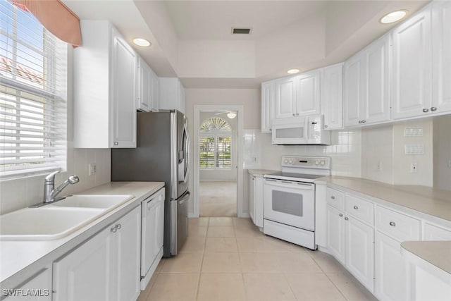 kitchen with white appliances, a sink, white cabinets, light tile patterned floors, and tasteful backsplash