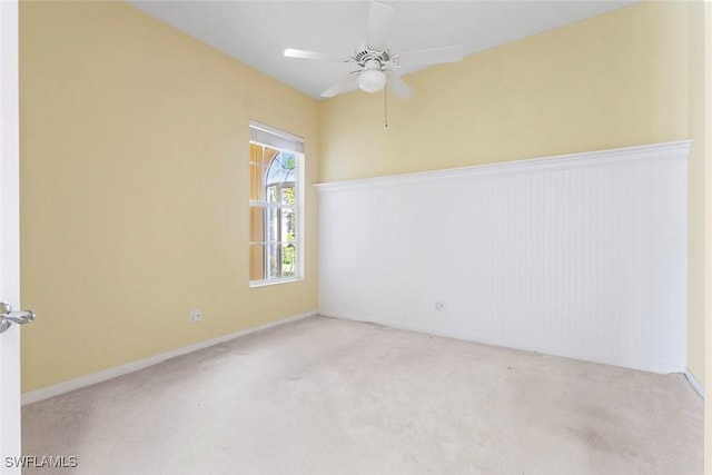 carpeted empty room featuring ceiling fan and a wainscoted wall
