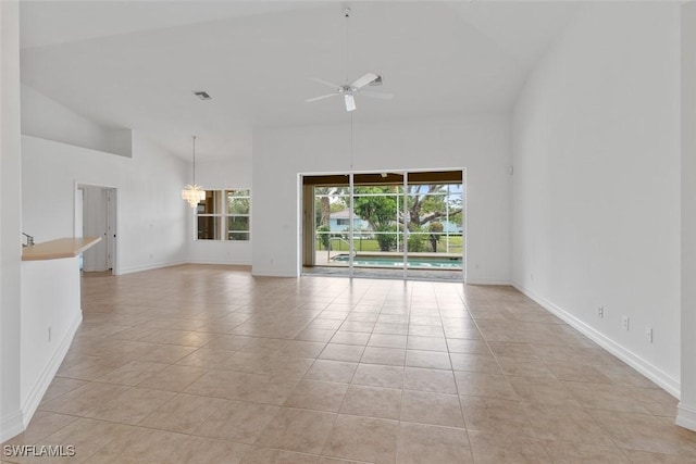 spare room featuring a ceiling fan, high vaulted ceiling, baseboards, light tile patterned flooring, and a chandelier