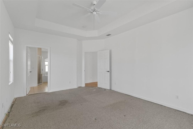 unfurnished bedroom featuring carpet, baseboards, a tray ceiling, and ensuite bathroom
