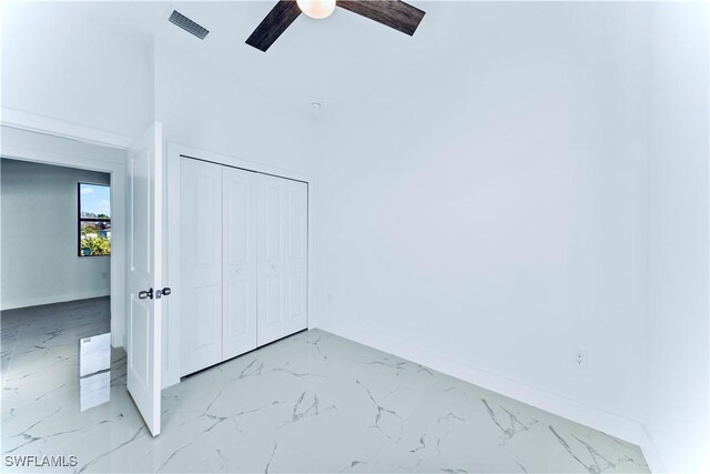 unfurnished bedroom featuring light marble finish floors, a closet, baseboards, and a ceiling fan