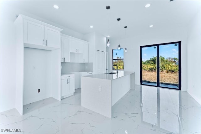 kitchen featuring a sink, recessed lighting, a kitchen island with sink, light marble finish flooring, and white cabinets
