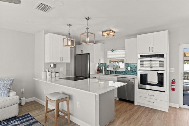 kitchen with stainless steel appliances, a sink, light wood-style flooring, a peninsula, and baseboards