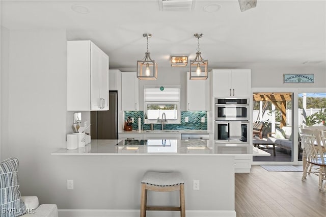 kitchen featuring stainless steel appliances, a sink, a peninsula, tasteful backsplash, and light countertops