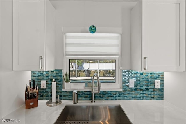 kitchen view of a sink, light countertops, white cabinets, and decorative backsplash