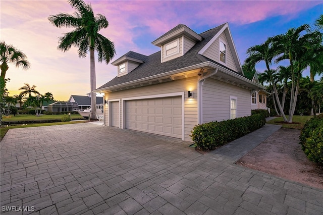27150 Mora Rd, Bonita Springs, FL 34135 - property exterior at dusk with decorative driveway, an attached garage, and roof with shingles