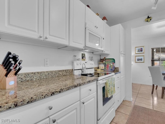 kitchen with white appliances, light tile patterned floors, white cabinets, light stone counters, and baseboards