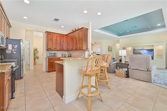 7810 Twin Eagle Ln, Fort Myers, FL 33912 - kitchen featuring light tile patterned flooring, brown cabinets, appliances with stainless steel finishes, a breakfast bar area, and a peninsula