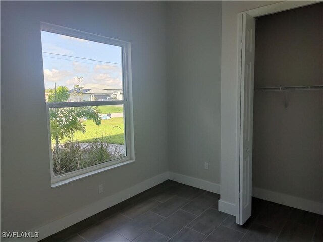 3607 SW 8th Ct, Cape Coral, FL 33914 - unfurnished bedroom featuring multiple windows, baseboards, dark tile patterned flooring, and a closet