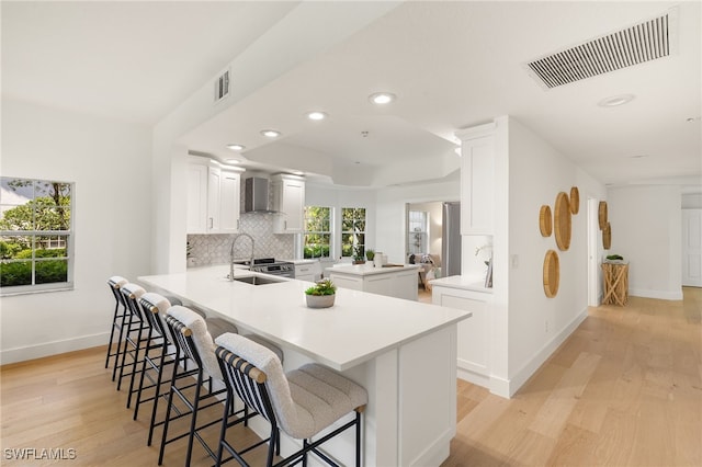 4485 Dover Ct Unit 1202, Naples, FL 34105 - kitchen featuring wall chimney range hood, light wood-type flooring, a breakfast bar area, a peninsula, and recessed lighting