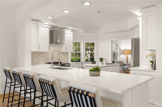 4485 Dover Ct Unit 1202, Naples, FL 34105 - kitchen with wall chimney range hood, a peninsula, tasteful backsplash, a breakfast bar, and recessed lighting
