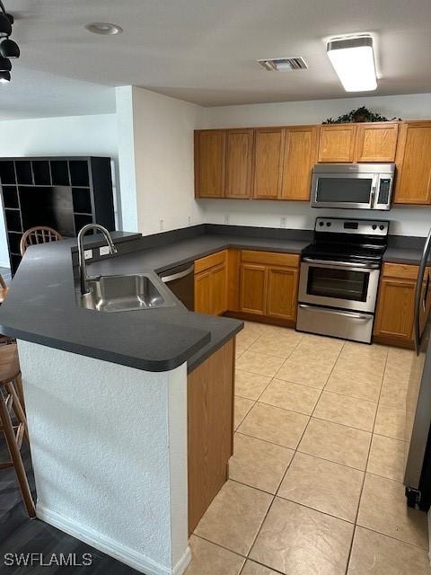 6370 Brant Bay Blvd Unit 105, North Fort Myers, FL 33917 - kitchen featuring stainless steel appliances, a sink, dark countertops, a peninsula, and brown cabinets