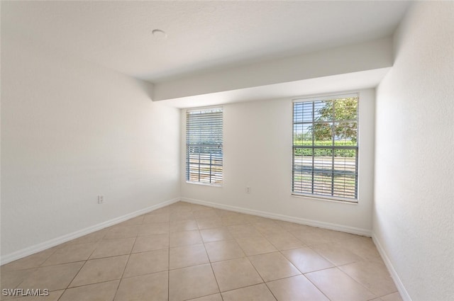spare room featuring healthy amount of natural light, light tile patterned floors, and baseboards