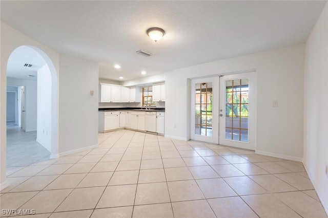 kitchen featuring white dishwasher, dark countertops, light tile patterned floors, baseboards, and arched walkways