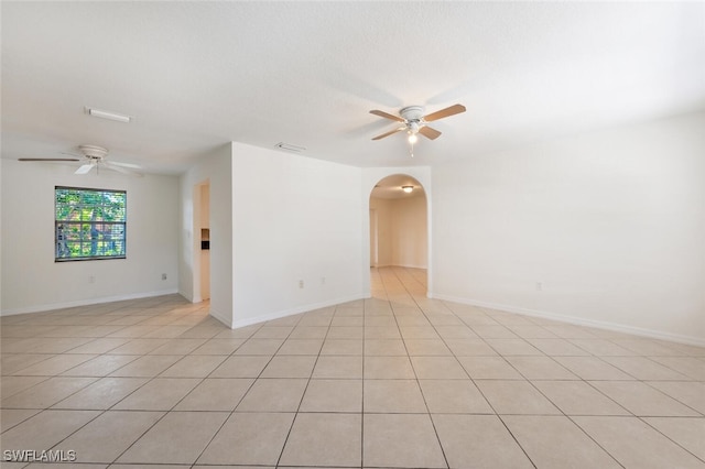 unfurnished room featuring a ceiling fan, arched walkways, and light tile patterned floors