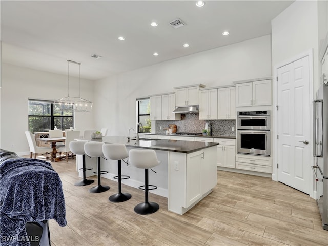 16289 Camden Lakes Cir, Naples, FL 34110 - kitchen with stainless steel double oven, under cabinet range hood, a sink, gas cooktop, and a breakfast bar
