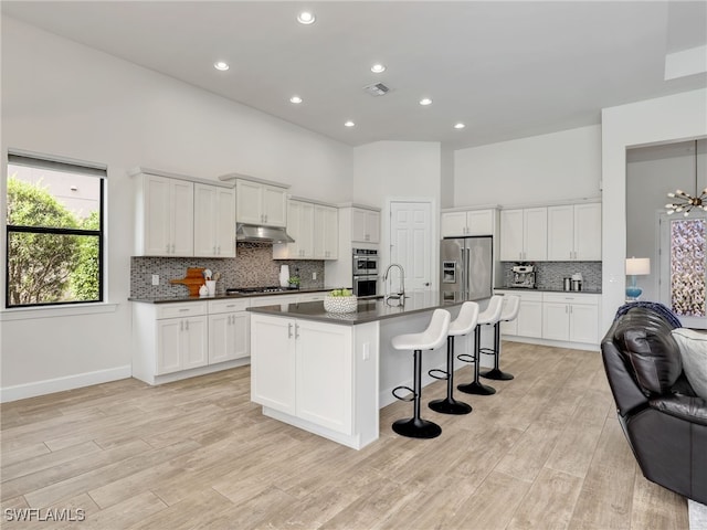 16289 Camden Lakes Cir, Naples, FL 34110 - kitchen with under cabinet range hood, stainless steel appliances, dark countertops, open floor plan, and a high ceiling