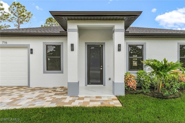 716 David Laird Ln, Lehigh Acres, FL 33974 - view of exterior entry featuring a shingled roof, stucco siding, and a garage