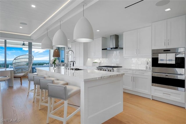 6897 Grenadier Blvd Unit 601, Naples, FL 34108 - kitchen with wall chimney exhaust hood, a sink, appliances with stainless steel finishes, light wood-style floors, and a wall of windows