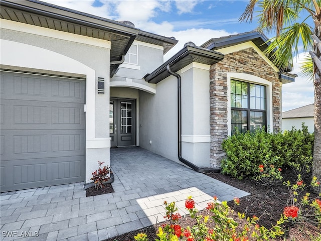 property entrance with stucco siding, stone siding, and a garage