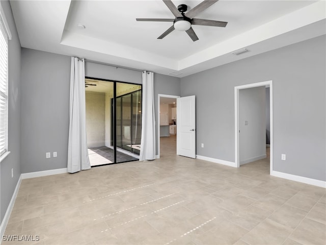 unfurnished bedroom featuring a raised ceiling, access to outside, ceiling fan, and baseboards