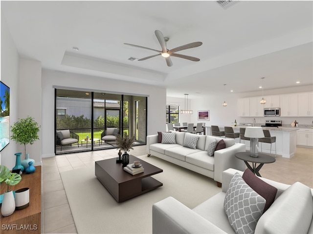 living area featuring ceiling fan, a tray ceiling, light tile patterned floors, and recessed lighting