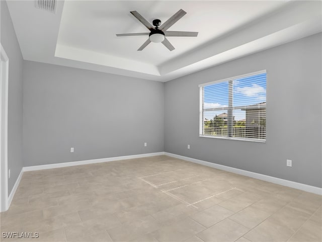 spare room with a tray ceiling, ceiling fan, and baseboards
