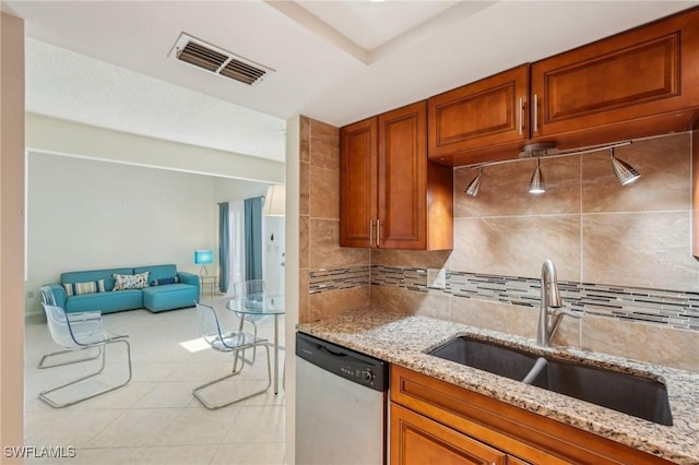 kitchen featuring dishwasher, light stone counters, a sink, brown cabinetry, and decorative backsplash