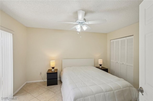 bedroom with a closet, light tile patterned floors, ceiling fan, baseboards, and a textured ceiling