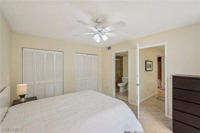 bedroom with two closets, light tile patterned flooring, ensuite bath, ceiling fan, and baseboards