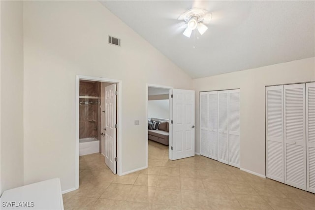 unfurnished bedroom featuring two closets, light tile patterned floors, baseboards, high vaulted ceiling, and connected bathroom