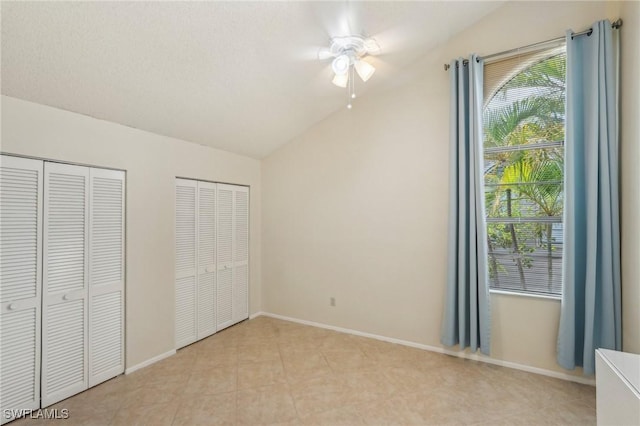 unfurnished bedroom with lofted ceiling, multiple closets, baseboards, light tile patterned floors, and a ceiling fan