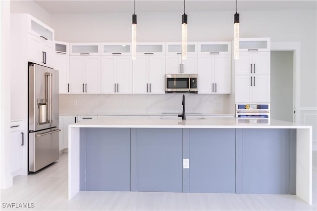2583 18th Ave SE, Naples, FL 34117 - kitchen featuring stainless steel appliances, a center island with sink, light countertops, and glass insert cabinets