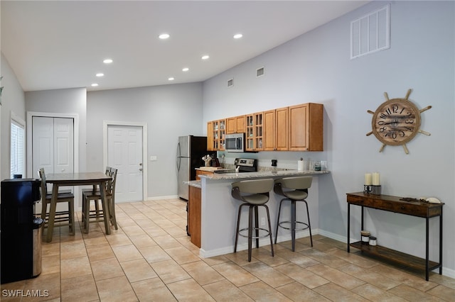 5211 Melaluca Dr, Fort Myers, FL 33905 - kitchen with stainless steel appliances, high vaulted ceiling, a peninsula, brown cabinetry, and a kitchen bar