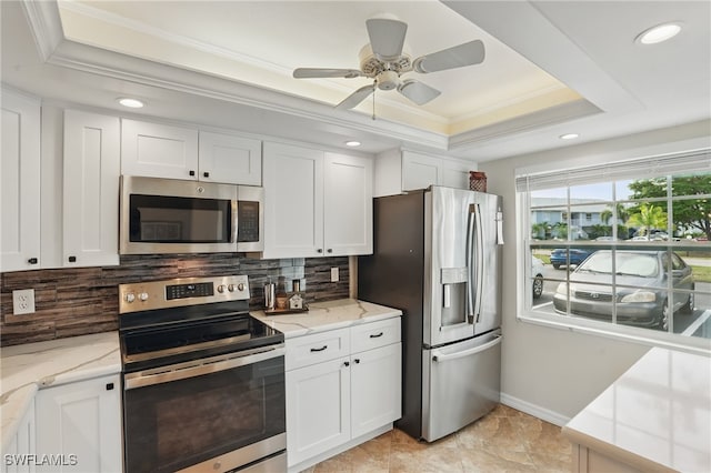 kitchen with appliances with stainless steel finishes, a raised ceiling, crown molding, white cabinets, and recessed lighting