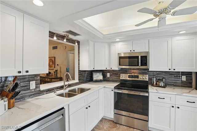 kitchen featuring appliances with stainless steel finishes, a sink, a tray ceiling, decorative backsplash, and white cabinets