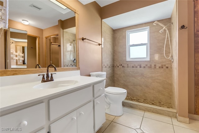 full bathroom featuring a tile shower, vanity, tile patterned flooring, and toilet