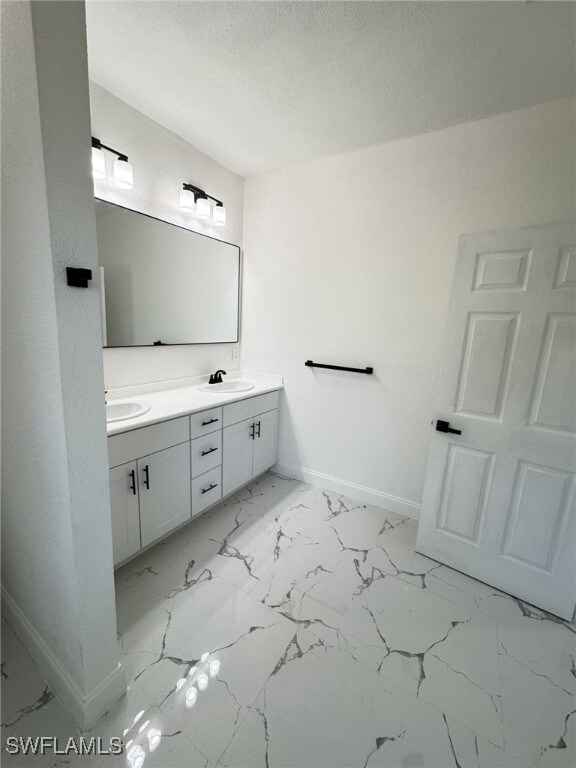 16 W 7th St, Lehigh Acres, FL 33972 - bathroom with baseboards, double vanity, marble look tile flooring, and a textured ceiling