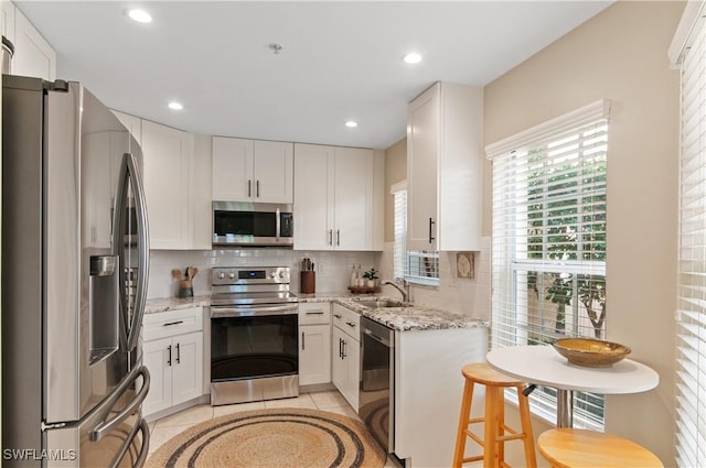 13020 Amberley Ct Unit 301, Bonita Springs, FL 34135 - kitchen with stainless steel appliances, decorative backsplash, light stone counters, white cabinets, and light tile patterned floors