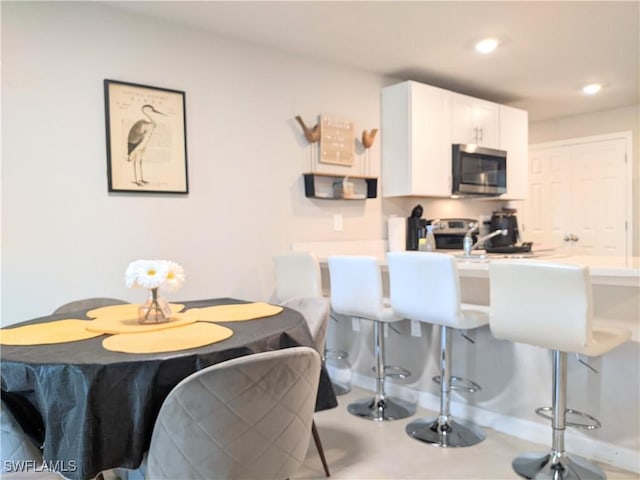 kitchen with stainless steel microwave, a kitchen breakfast bar, stove, white cabinets, and recessed lighting