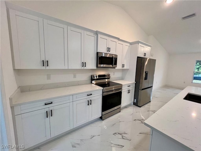 kitchen featuring stainless steel appliances, lofted ceiling, light marble finish flooring, light stone counters, and white cabinetry