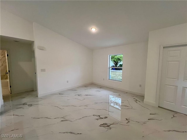 unfurnished room featuring baseboards, vaulted ceiling, and light marble finish flooring