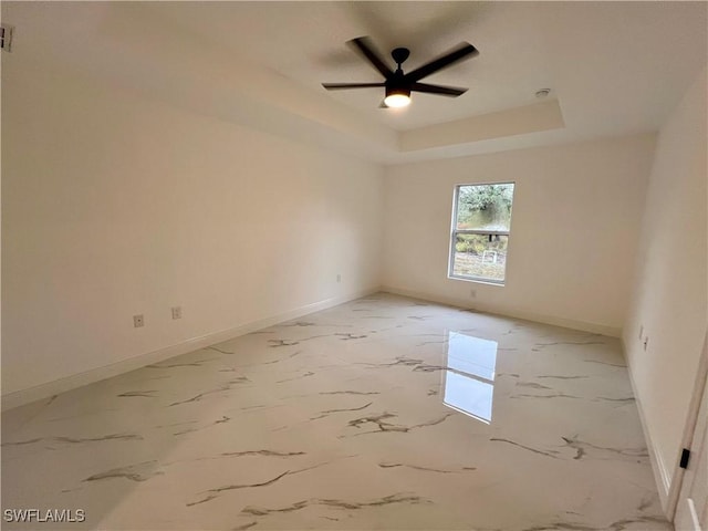 spare room with baseboards, ceiling fan, a raised ceiling, and light marble finish floors
