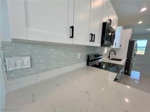 kitchen featuring stainless steel appliances, a sink, white cabinets, backsplash, and light stone counters