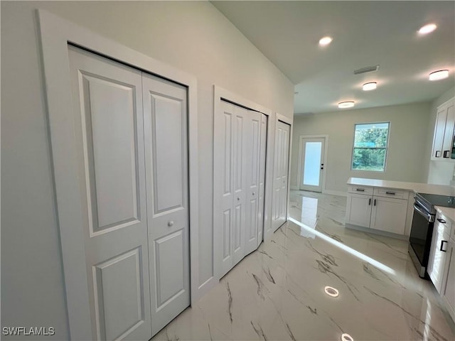 kitchen with light marble finish floors, white cabinets, black electric range oven, recessed lighting, and light countertops