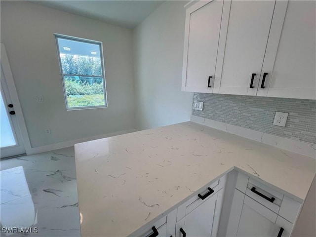 kitchen featuring backsplash, white cabinets, marble look tile flooring, and light stone counters
