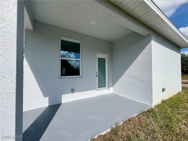 view of exterior entry featuring stucco siding and a patio