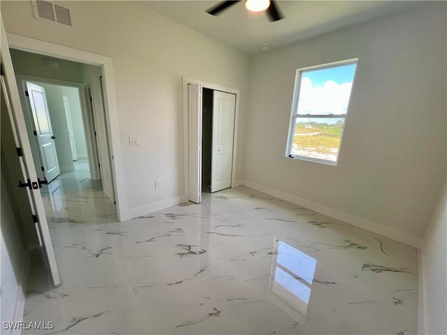 unfurnished bedroom with baseboards, a closet, light marble finish floors, and a ceiling fan