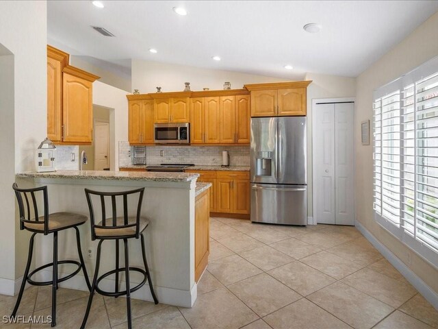 7930 Wexford Dr, Naples, FL 34104 - kitchen featuring stainless steel appliances, lofted ceiling, tasteful backsplash, light stone countertops, and plenty of natural light